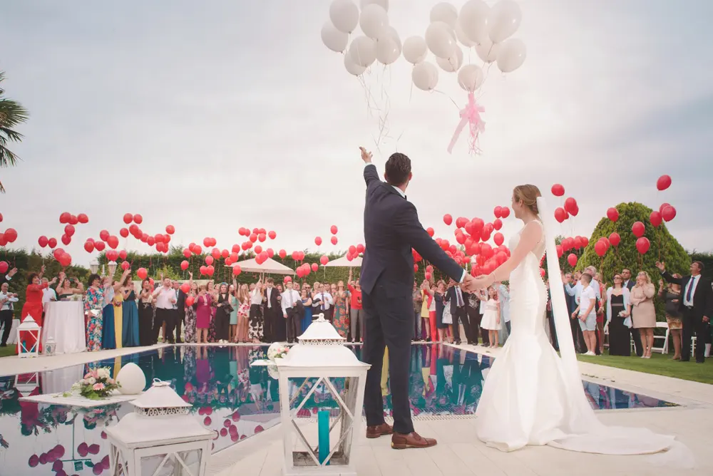 Los novios soltando globos junto a la alberca, rodeados de invitados
